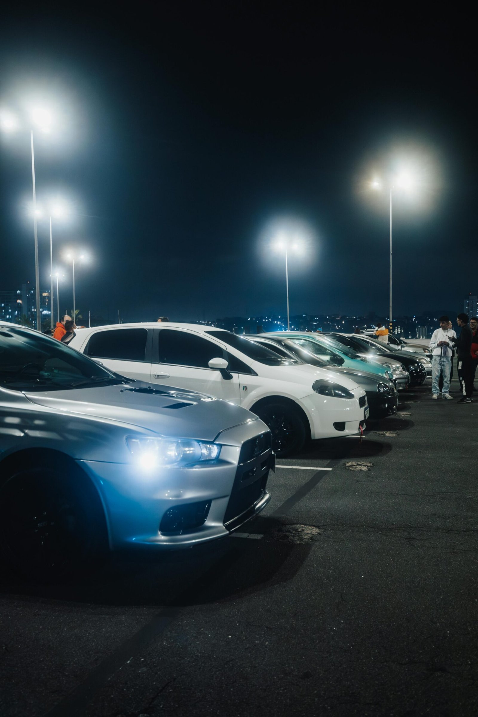 A vivid night scene capturing a row of cars parked under bright streetlights in a spacious parking lot.